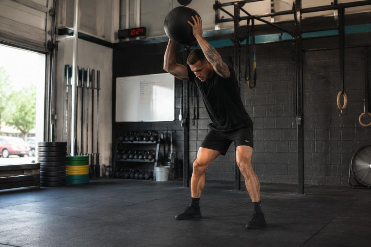 A trainer demonstrating a slam ball exercise in a small CrossFit box