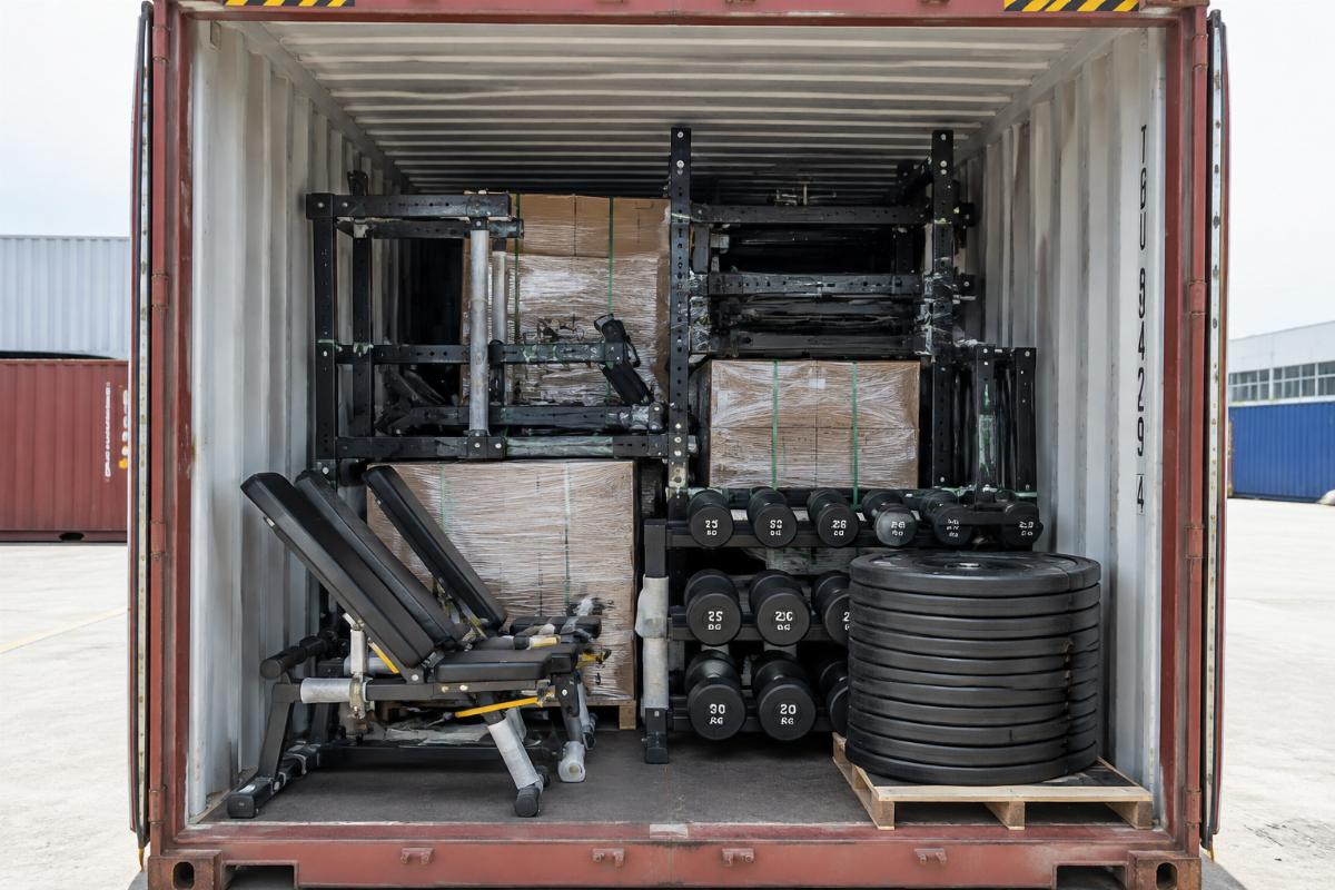 Mixed container load of commercial gym equipment including adjustable benches, racks, and free weights
