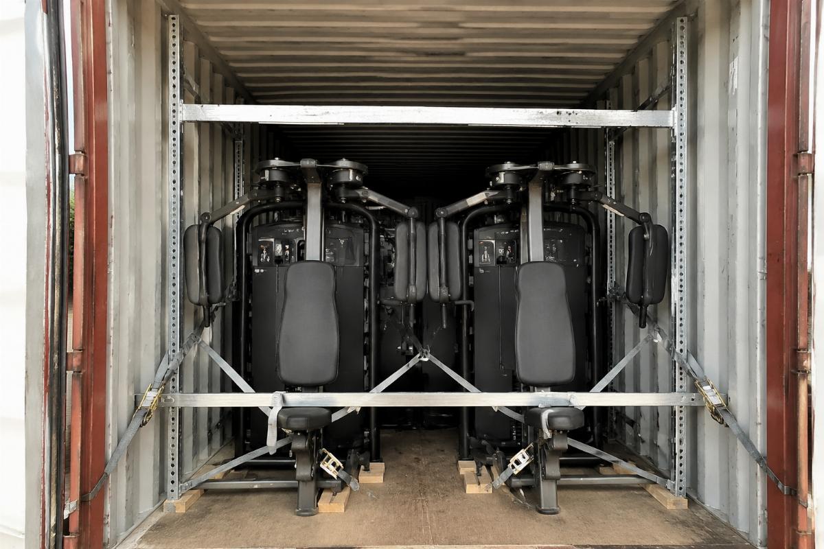 Pec Deck machines loaded inside a shipping container with visible guide rail bracing and frame tie-downs
