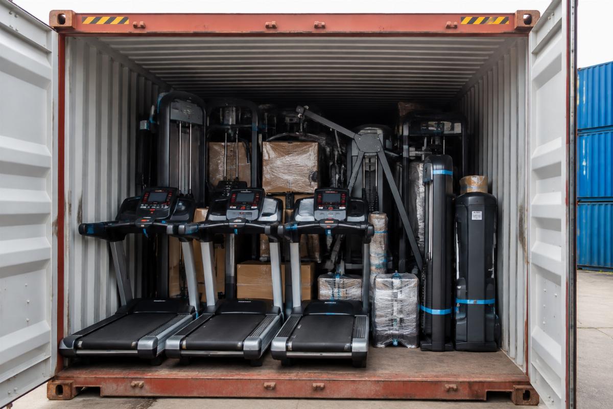 Shipping container loaded with commercial gym equipment including treadmills and strength machines