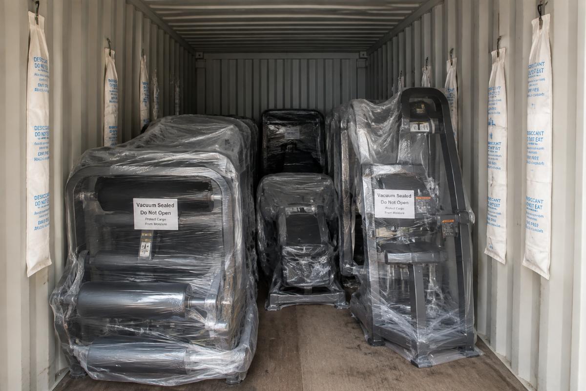 Vacuum-sealed fitness equipment inside a shipping container with hanging desiccant strips visible on the container walls